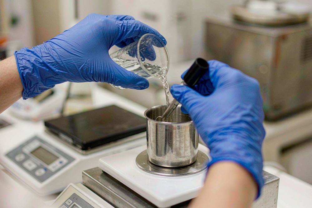 Technician weighing and mixing a two-component epoxy batch on a laboratory balance