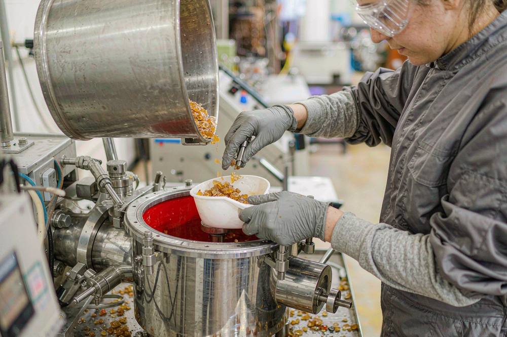 worker in protective overalls and gloves charging amber solid resin flakes into a heated stainless steel vessel